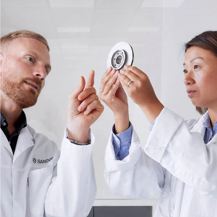 Man and woman in white coats inspecting a metal disc (photo)