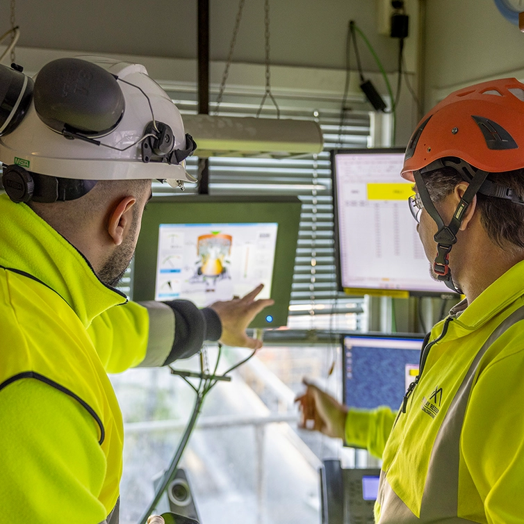 Två personer med hjälmar tittar på en dataskärm. (foto)